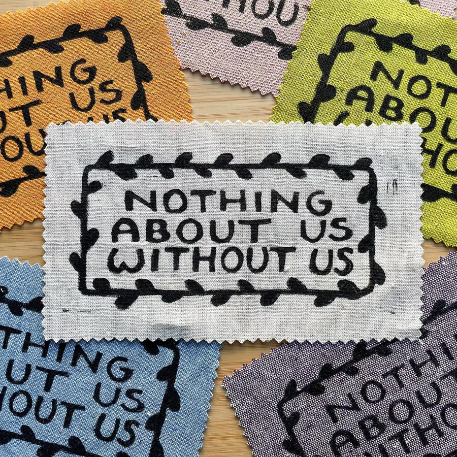 Block printed patches that read "Nothing About Us Without Us"